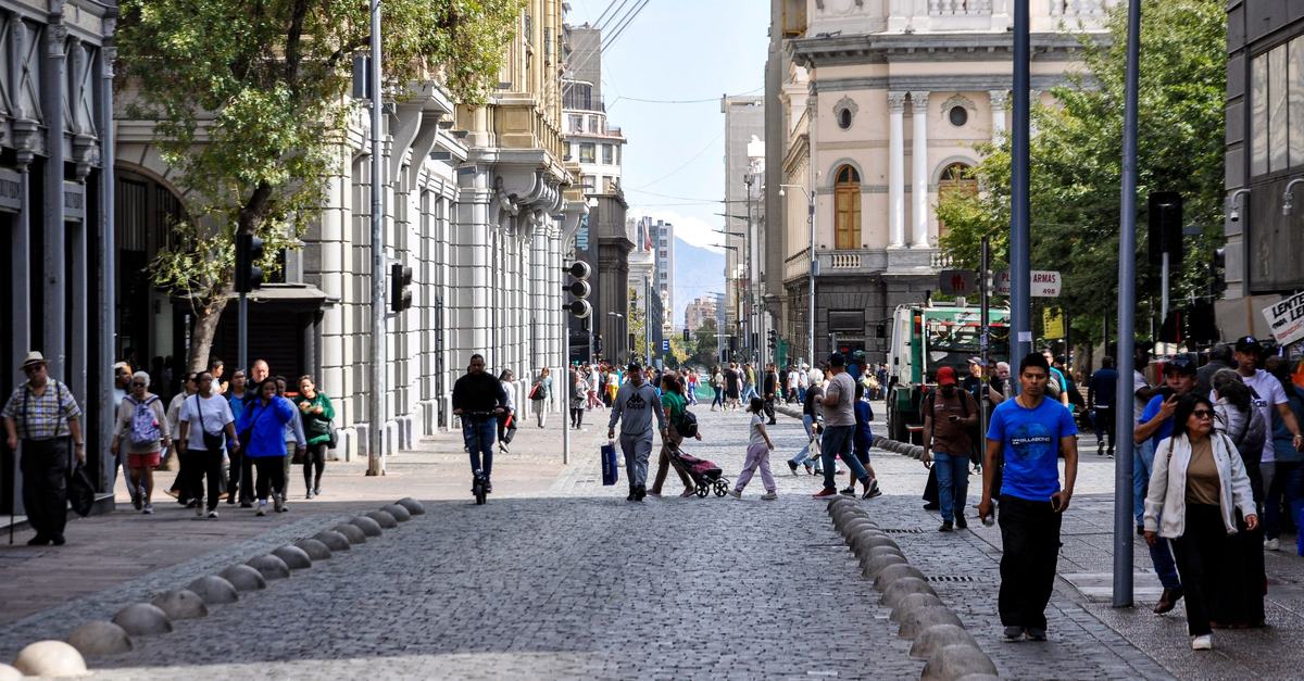 Peatones recorren un paseo del centro histórico de Santiago, entre edificios patrimoniales y comercio, en un día soleado